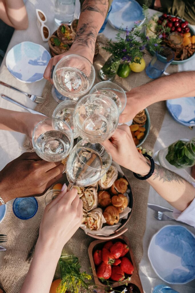 A cheerful group clinks glasses during an outdoor brunch celebration, with diverse hands and appetizing food.