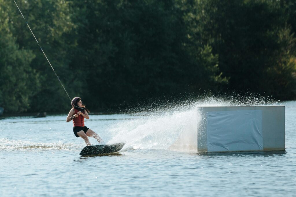 A woman skillfully wakeboards across a lake, splashing water under a bright summer sky.